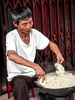 Pria memakai kaus putih memasak dengan wajan di dapur